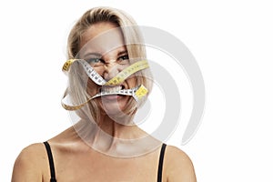 Angry young blonde woman with a measuring tape in her mouth. Isolated on white background. Space for the test. Efforts for a