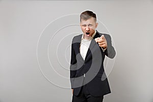 Angry young business man in classic black suit, shirt swearing screaming, pointing index finger on camera isolated on