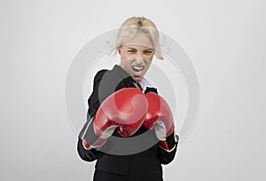 Angry young businesswoman in boxing gloves ready for fight over light grey background, preparing for combat