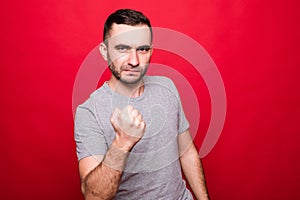 Angry young Caucasian man show clenched fist threaten or give warning isolated on red studio background demonstrate threat or