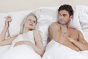 Angry young couple looking at each other in bed