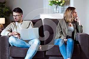 Angry young couple sitting on sofa together and looking to opposite sides at home.