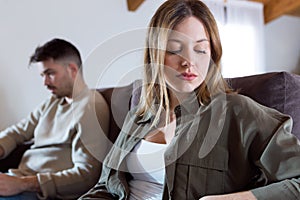 Angry young couple sitting on sofa together and looking to opposite sides at home.