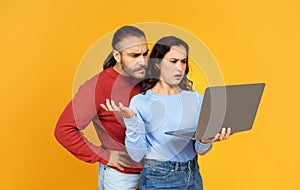 Angry young couple using modern laptop on yellow