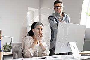 Angry young european man boss scolds to frightened shocked sad manager lady at workplace with computer