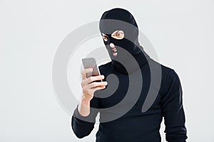 Angry young man in balaclava using cell phone