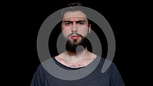 Angry young man with beard makes disagree sign by shaking his head, isolated on black background. Handsome man wearing