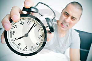 Angry young man in bed holds his alarm clock