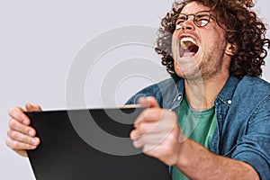 Angry young man with curly hair sitting at his desk with laptop feeling stressed.