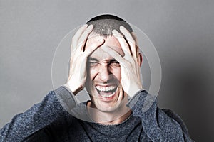 Angry young man holding his head, screaming his burnout