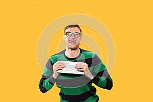 Angry young man holding a keyboard in his hands and trying to break it on yellow background. Studio photo