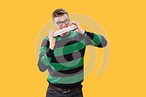 Angry young man holds a keyboard in his hands and bites it on yellow background