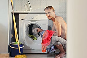 Angry young man loads the laundry into the washing machine. Male housewife or bachelor concept