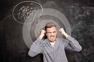 Angry young man in rage standing against the background of chalkboard