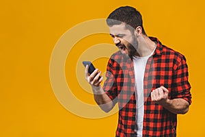 Angry young man screaming on the cell phone isolated on a yellow background