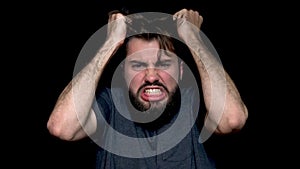 Angry young man shouting, expressing negative emotions, tearing his hair out, isolated on black background. Close up of