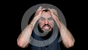 Angry young man shouting, expressing negative emotions, tearing his hair out, isolated on black background. Close up of