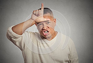 Angry young man showing loser sign on forehead