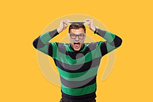 Angry young man trying to break the keyboard on his head and screaming hard on yellow background