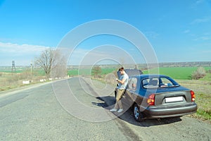 Angry young man waiting a help while sitting near the broken car