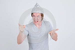 Angry young man wearing tin foil hat as conspiracy theory concept pointing finger