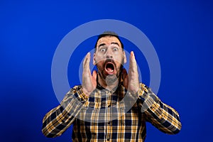 Angry young man yelling screaming. Hipster man with beard in blue plaid checkered shirt Isolated on gray studio