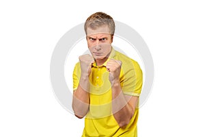 Angry young man in yellow T-shirt ready to fight with fists isolated on white background