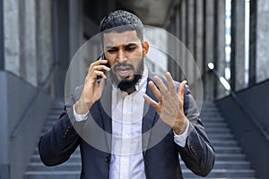 Angry young Muslim businessman talking on the phone near an office building