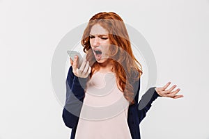 Angry young redhead lady talking by mobile phone and screaming.