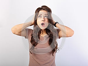 Angry young surprising business woman holding the head the hands with big eyes looking up. Fun humor casual portrait on light blue