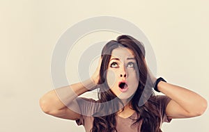 Angry young surprising business woman holding the head the hands with big eyes and open mouth looking up. Fun humor casual