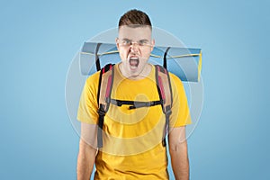 Angry young traveler with rucksack screaming on blue studio background