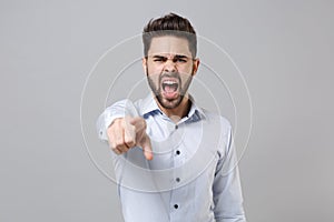 Angry young unshaven business man in light shirt posing isolated on grey background. Achievement career wealth business