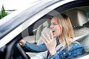 Angry young woman driver sitting in car, shouting.