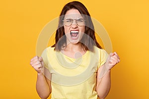 Angry young woman in glasses screaming with wild expression, being very upset, has dark hair, yelling frantically, brunette lady
