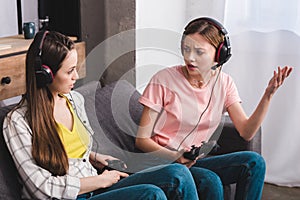 angry young woman in headphones with joystick in hand quarreling with female friend