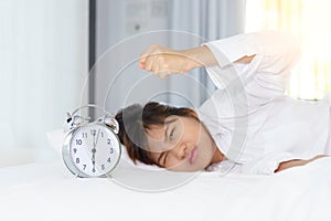 Angry young woman looking at alarm clock with clench one`s hand