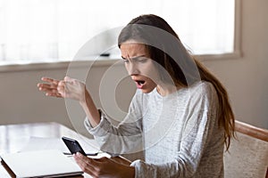 Angry young woman looking on mobile phone screen having problems