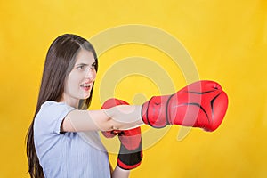 Angry young woman with red boxing gloves stands in fighting position, punching with hand. Portrait of strong and determined girl
