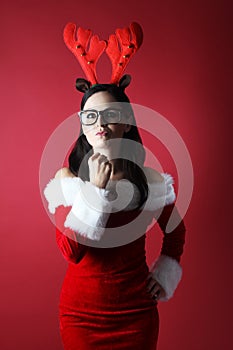 Angry young woman with reindeer attire and glasses and santan in santa helper hat with gift box front of red background