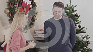 Angry young woman shouting at her husband or boyfriend. Couple arguing in front of Christmas tree on New Year`s eve