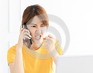 Angry young woman  shouting on mobile phone while working on  laptop