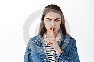 Angry young woman shushing, frowning and make shhh hush gesture with finger on lips, taboo sign, tell to be quiet