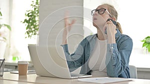 Angry Young Woman Talking on Phone while using Laptop