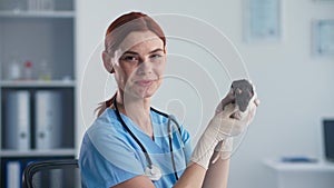 animal care, young female doctor in medical holds little cute mouse, smiles and looks at camera in office of veterinary