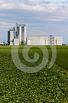 An animal feed production plant against the background of green agricultural fields.