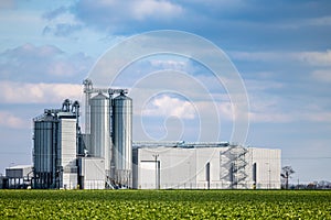 An animal feed production plant against the background of green agricultural fields.