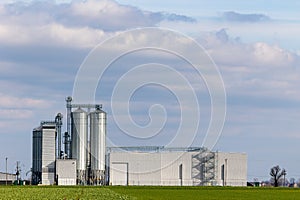 An animal feed production plant against the background of green agricultural fields.