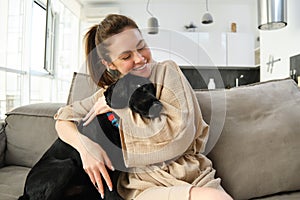 Animals and lifestyle concept. Happy young woman in bathrobe, hugs her dog on sofa, cuddle puppy and smiling