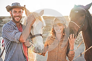 Animals lovers couple taking with bitless horses during sunny day inside ranch corral - Happy people having fun training at their